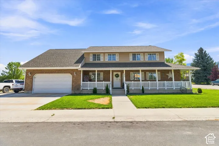 Two-story residence featuring brick and siding exterior, expansive covered front porch with white railing, and attached two-car garage