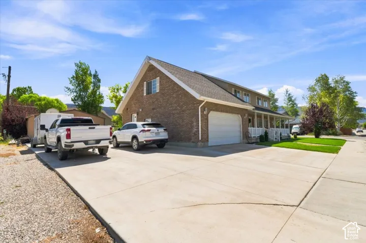 Brick exterior featuring a gabled roof, an attached two-car garage, and a covered front porch with white railings