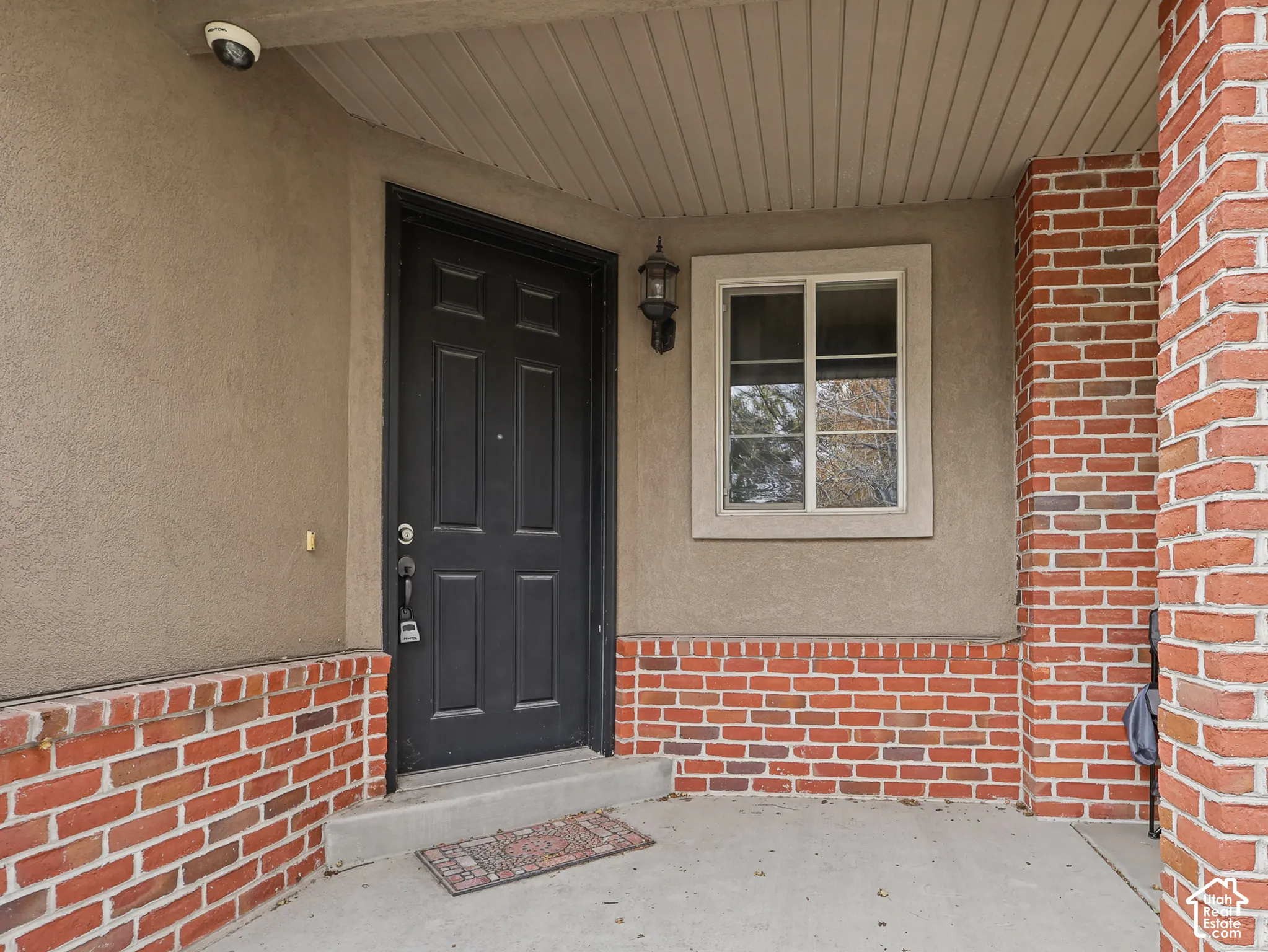 Covered entry featuring a brick facade, stucco exterior, solid panel door, and wall-mounted sconce