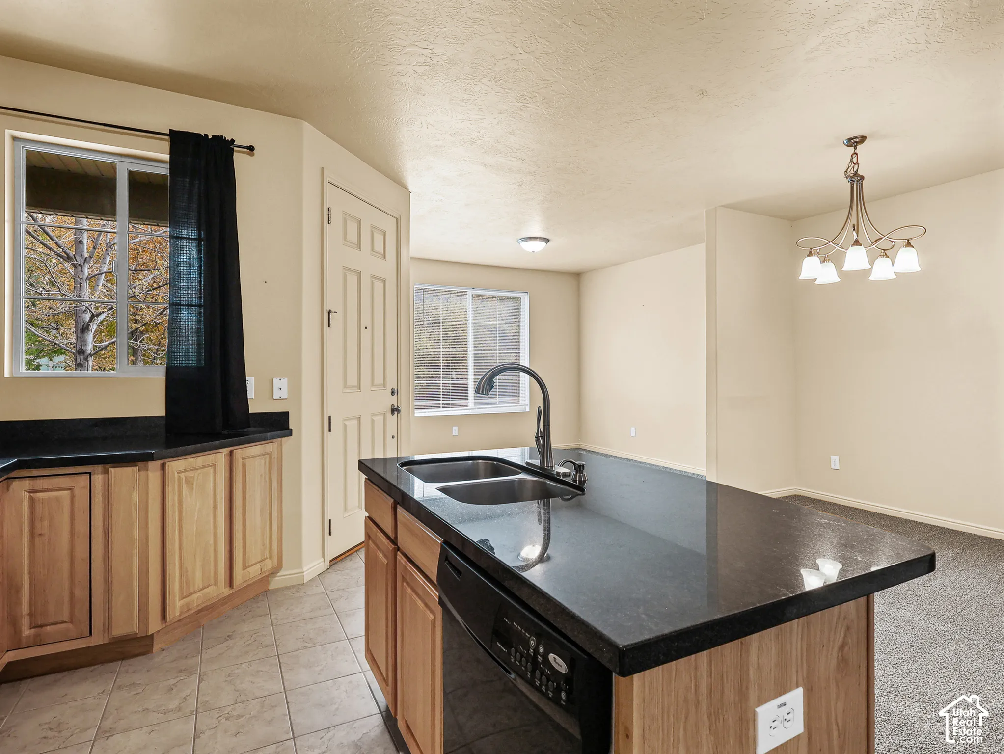Kitchen featuring a center island, dark stone-finish countertops, light wood cabinetry, a dual-basin undermount sink with a gooseneck faucet, and a multi-light chandelier