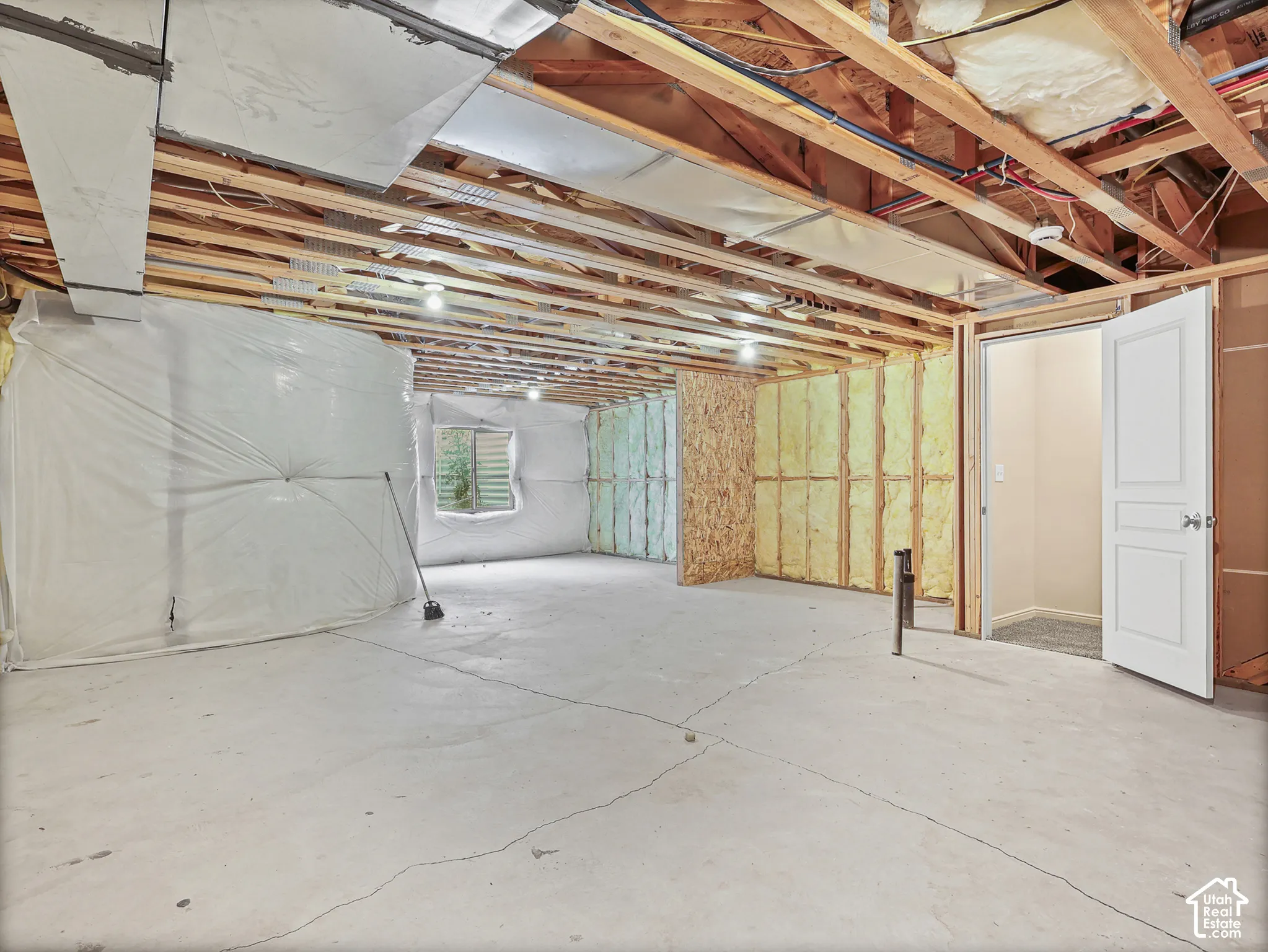 Unfinished interior space featuring exposed wood joists, concrete flooring, exterior-grade wall insulation, and a multi-panel interior door