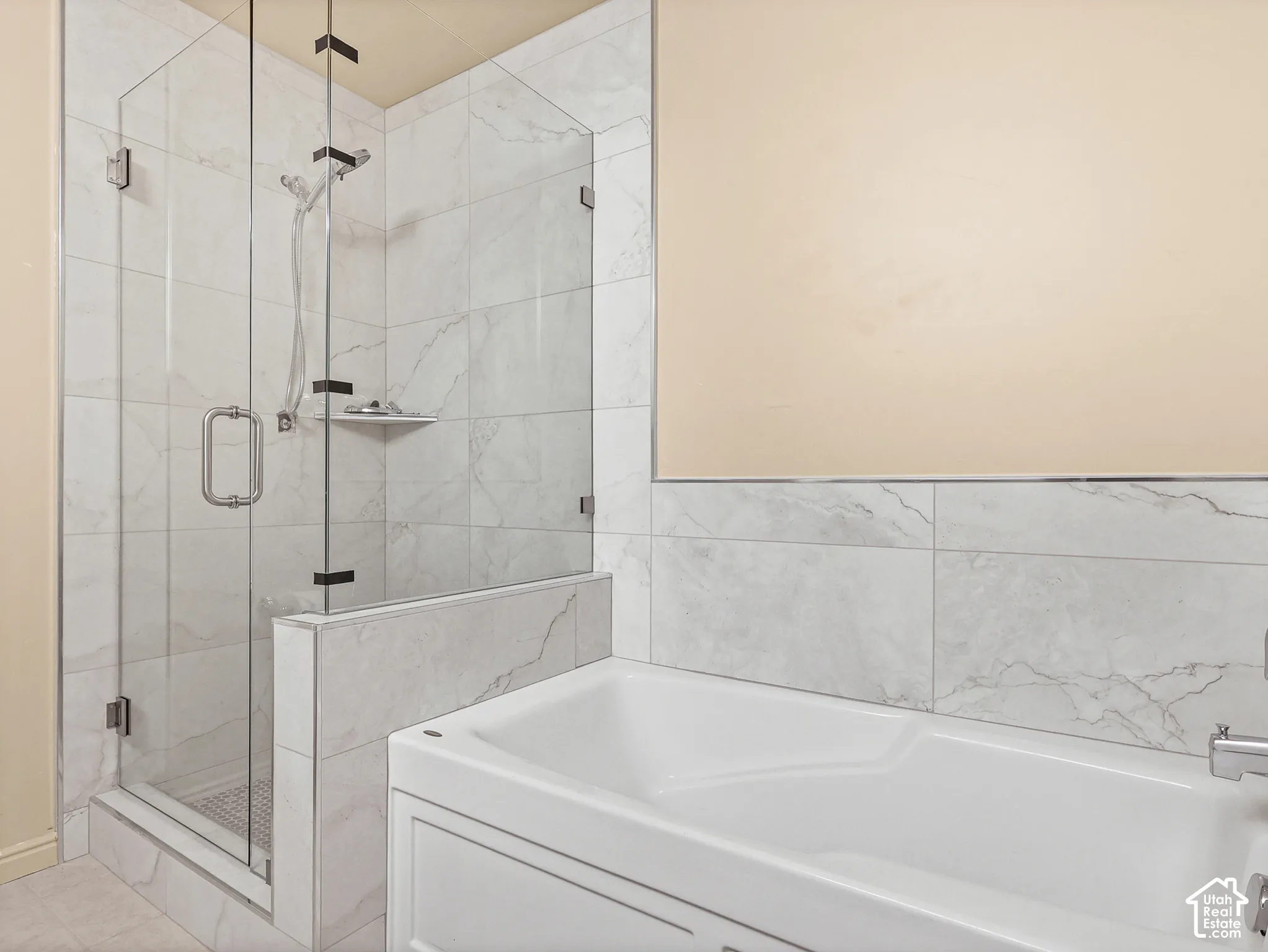 Walk-in shower featuring a frameless glass enclosure, handheld shower fixture, and stone-finish tile surround, paired with a white soaking tub