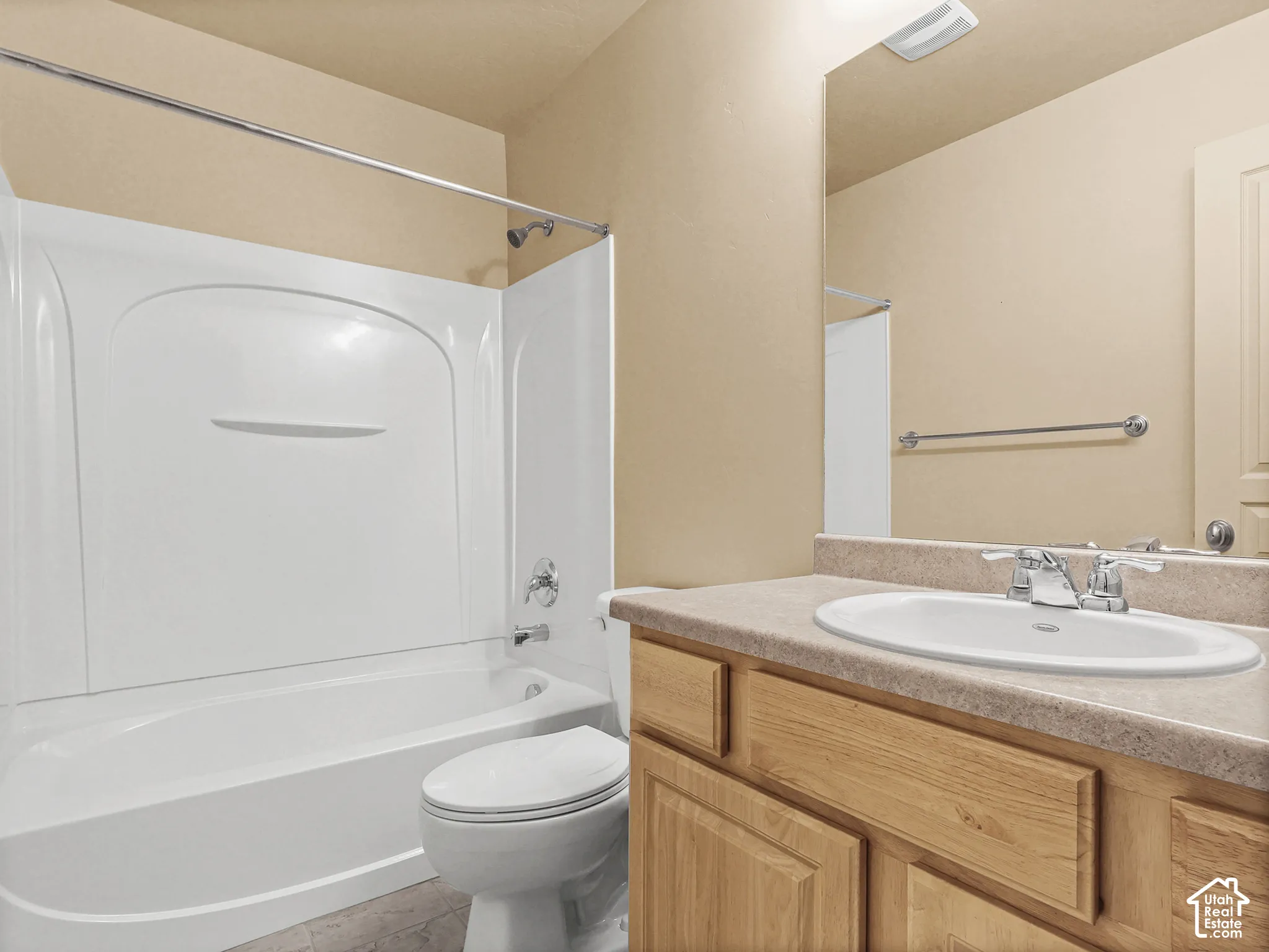 Bathroom featuring a wood-finish vanity with a molded countertop and integrated sink, a large wall-mounted mirror, and a tub-shower combination with a surround enclosure