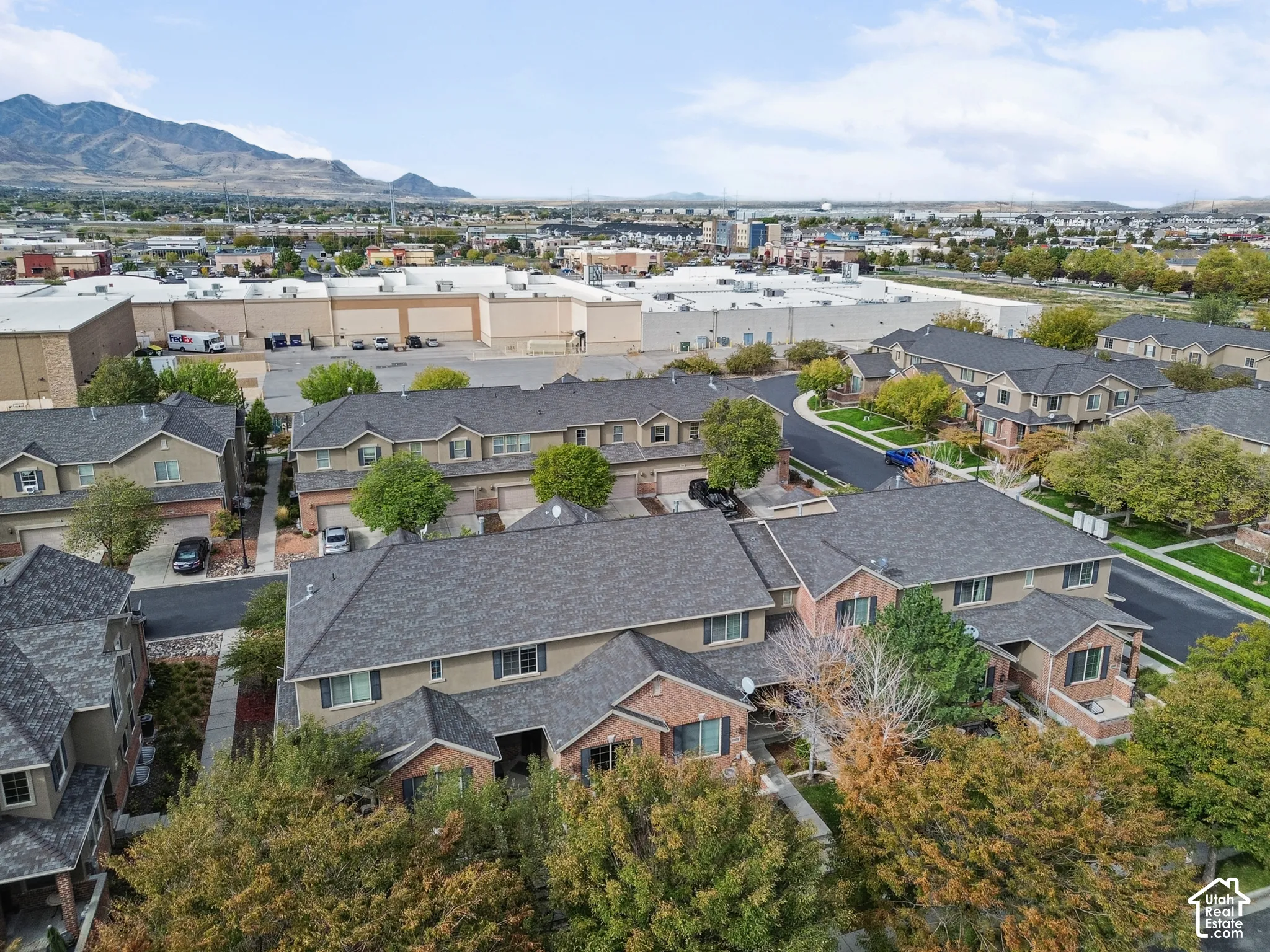 Multi-level residential complex featuring multi-tone brick and siding exterior, architectural shingle roofing, and paved driveway access, set against a mountain backdrop