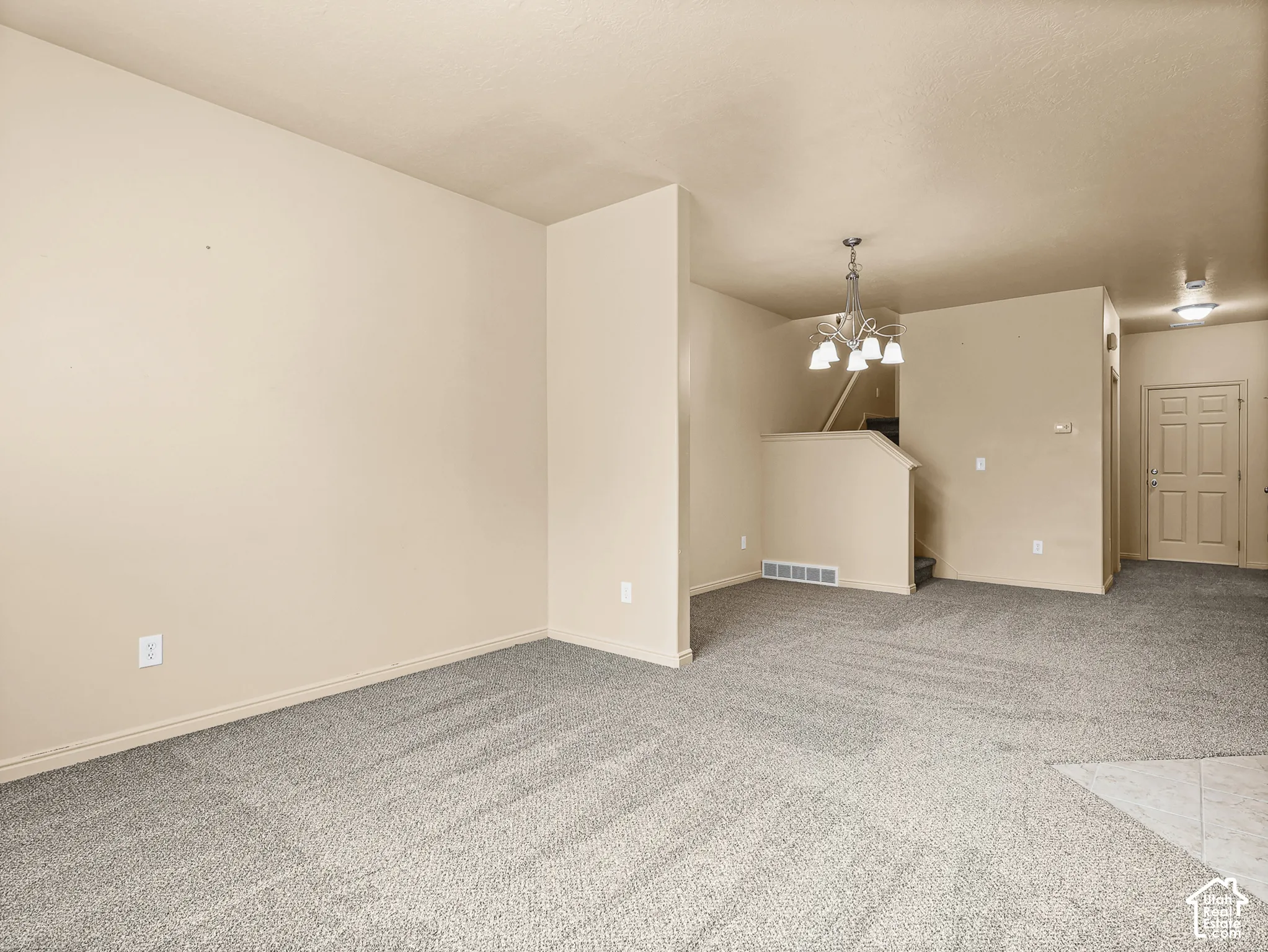 Neutral-toned interior featuring wall-to-wall carpeting, a multi-arm chandelier, and a paneled entry door