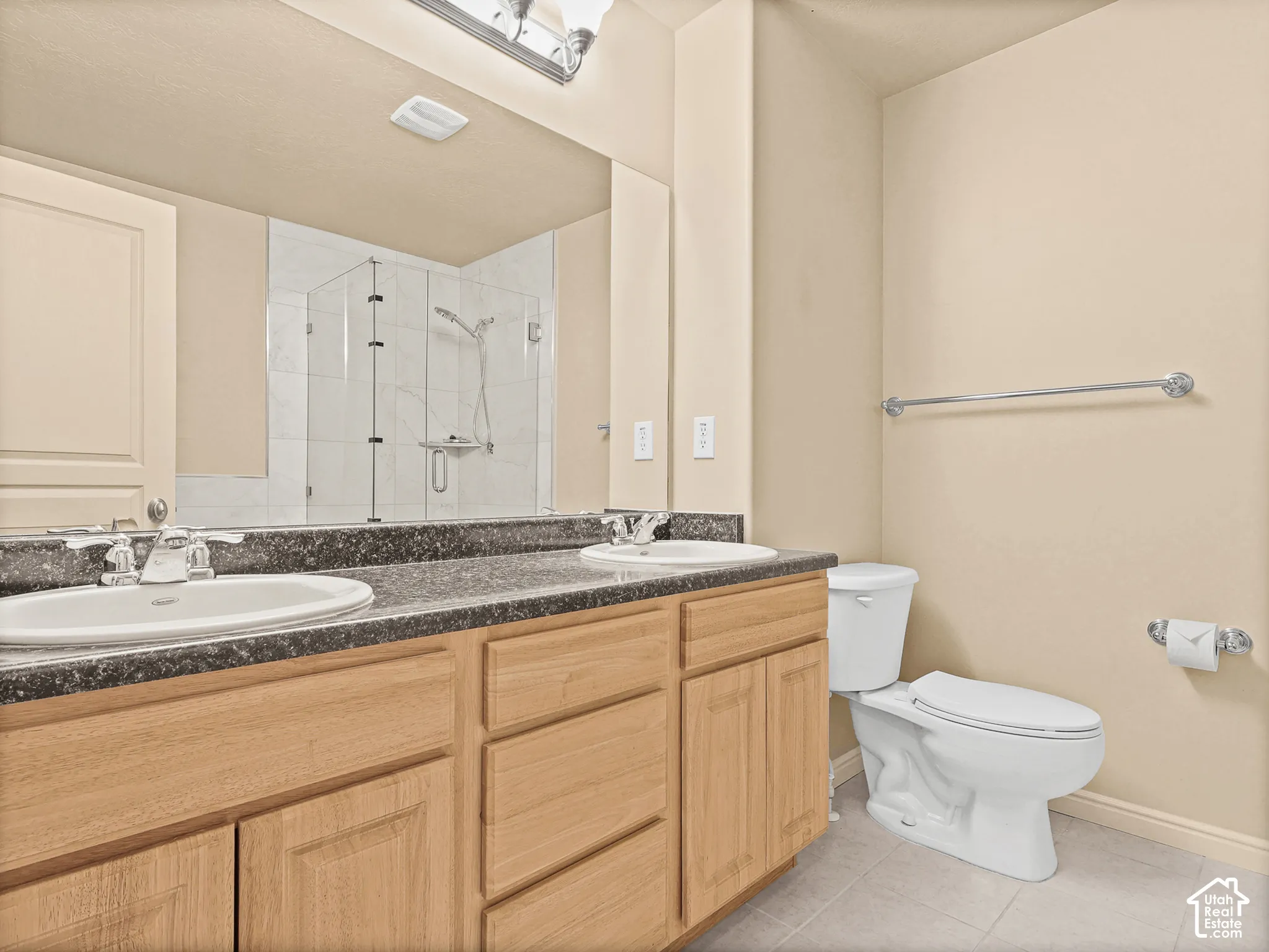 Dual-sink vanity with stone-finish countertop, wood-finish cabinetry, full-width vanity mirror, and glass-enclosed shower with tiled surround