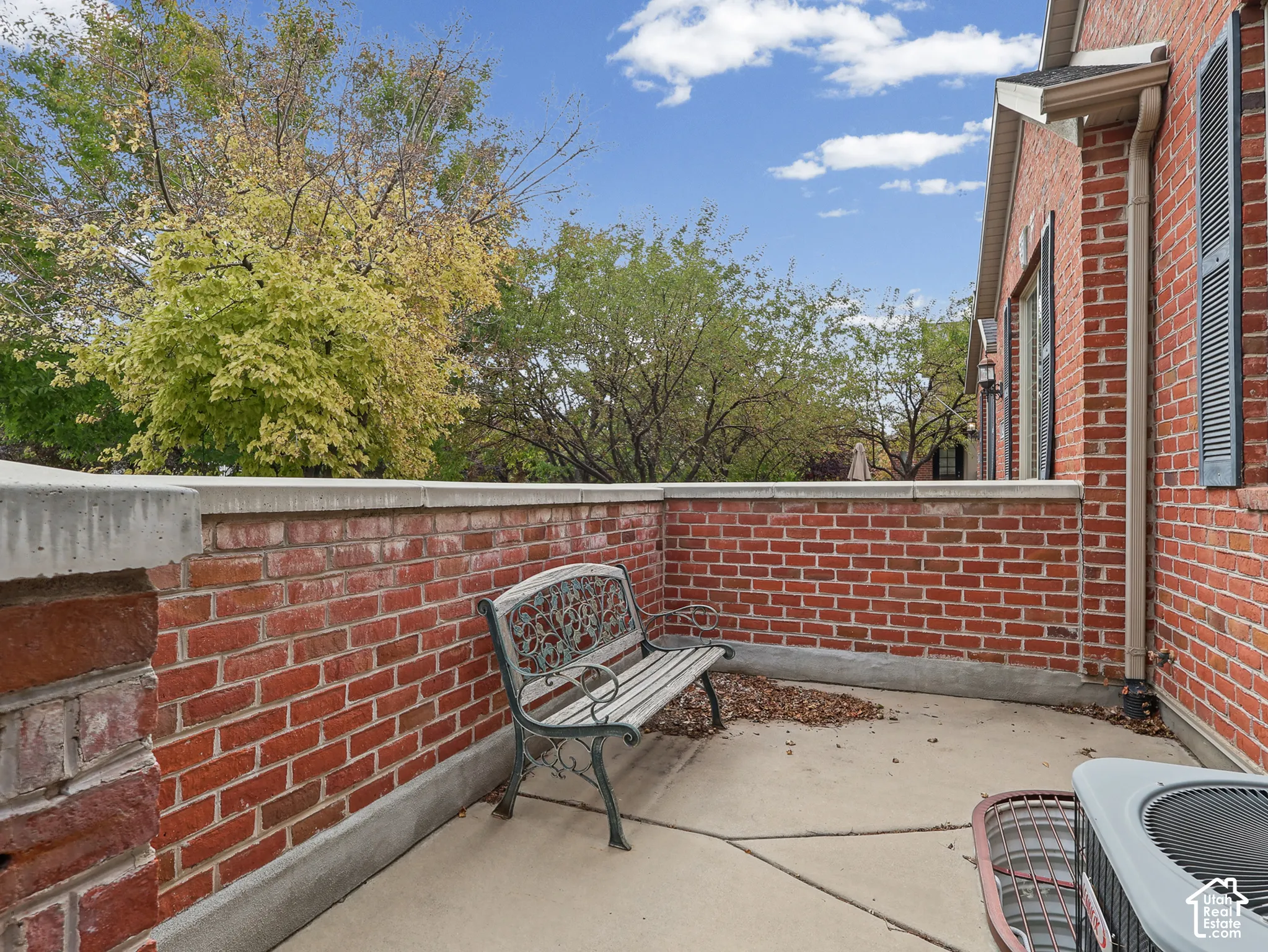 Exterior brick patio featuring a low-profile masonry wall, concrete surface, and mature perimeter trees