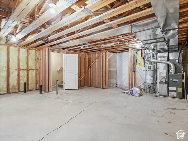 Unfinished lower level featuring exposed wood-framed walls, concrete flooring, and metal HVAC ductwork, including an integrated water heater and forced-air furnace system