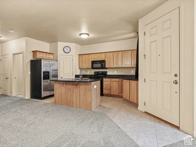 Kitchen featuring natural wood-finish cabinetry, a center island with a stone countertop, dark stone-surface countertops, and built-in stainless steel appliances