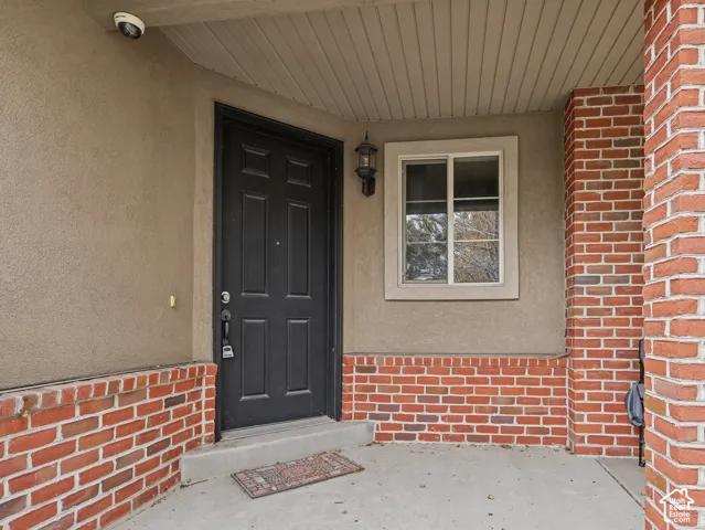 Covered entry featuring a brick facade, stucco exterior, solid panel door, and wall-mounted sconce