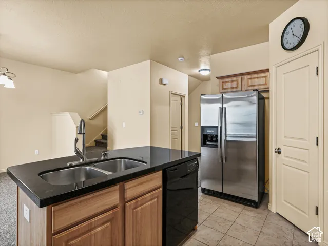 Kitchen island featuring a dual-basin stainless steel sink with a high-arch faucet, dark solid-surface countertop, and natural wood cabinetry