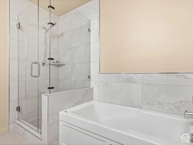Walk-in shower featuring a frameless glass enclosure, handheld shower fixture, and stone-finish tile surround, paired with a white soaking tub