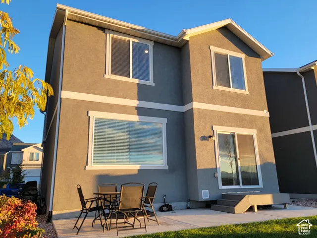 Two-story exterior featuring textured stucco siding, white trim detailing, a concrete rear patio, and a sliding glass door