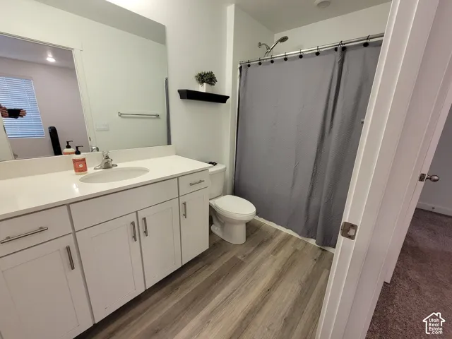 Bathroom featuring white cabinetry, integrated countertop with oval basin, large wall-mounted mirror, wood-finish flooring, and a shower-tub combination