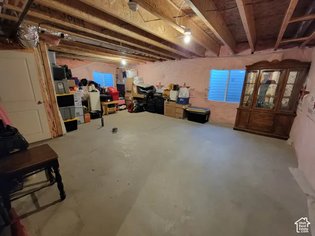 Unfinished basement space featuring exposed wood ceiling joists, concrete flooring, and windows with integrated security bars
