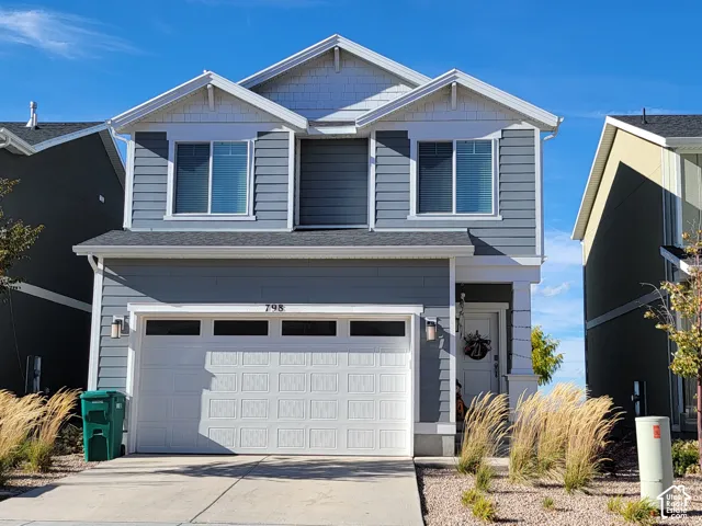 Two-story residence featuring grey horizontal lap siding, white trim accents, gabled rooflines with shake siding detailing, and a multi-panel garage door with transom windows