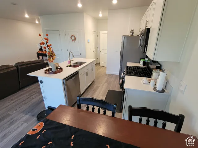 Kitchen featuring white cabinetry, wood-finish flooring, a central island with a double-basin sink, and recessed lighting