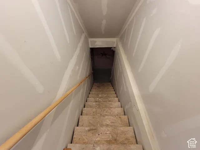 Staircase featuring unfinished oriented strand board treads and a natural wood handrail flanked by drywall with taped seams