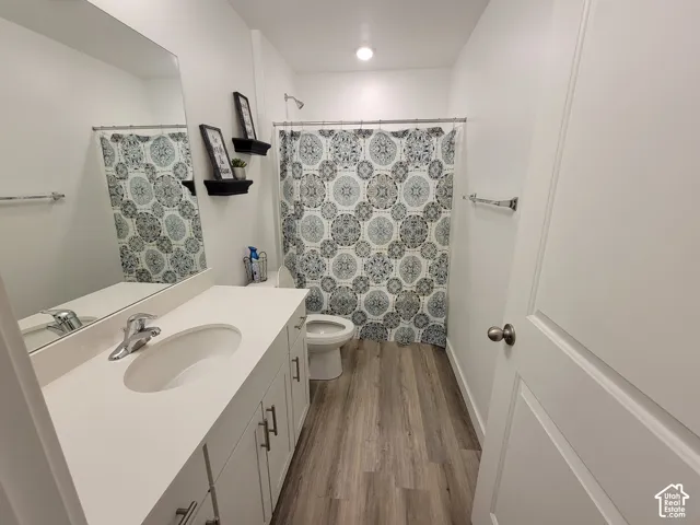 Bathroom featuring wood-finish flooring, white cabinetry with silver-tone hardware, a solid-surface countertop with an integrated basin, and a full-width vanity mirror