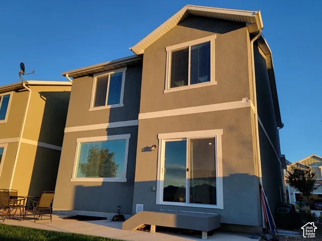 Two-story residence with a stucco exterior, gabled roofline, sliding glass door, and a concrete rear patio