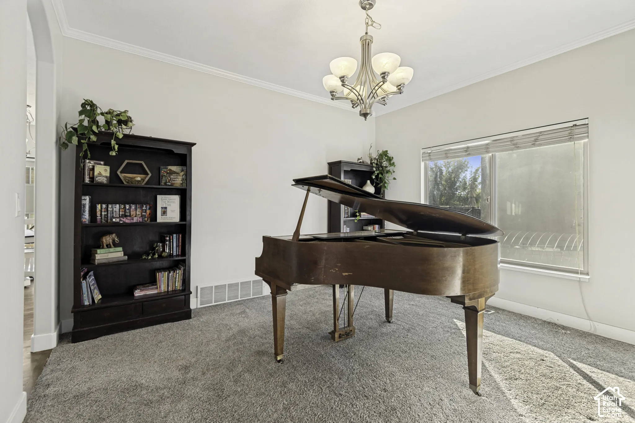 Room featuring crown molding, neutral carpeting, a multi-light polished nickel chandelier, and a large horizontal window