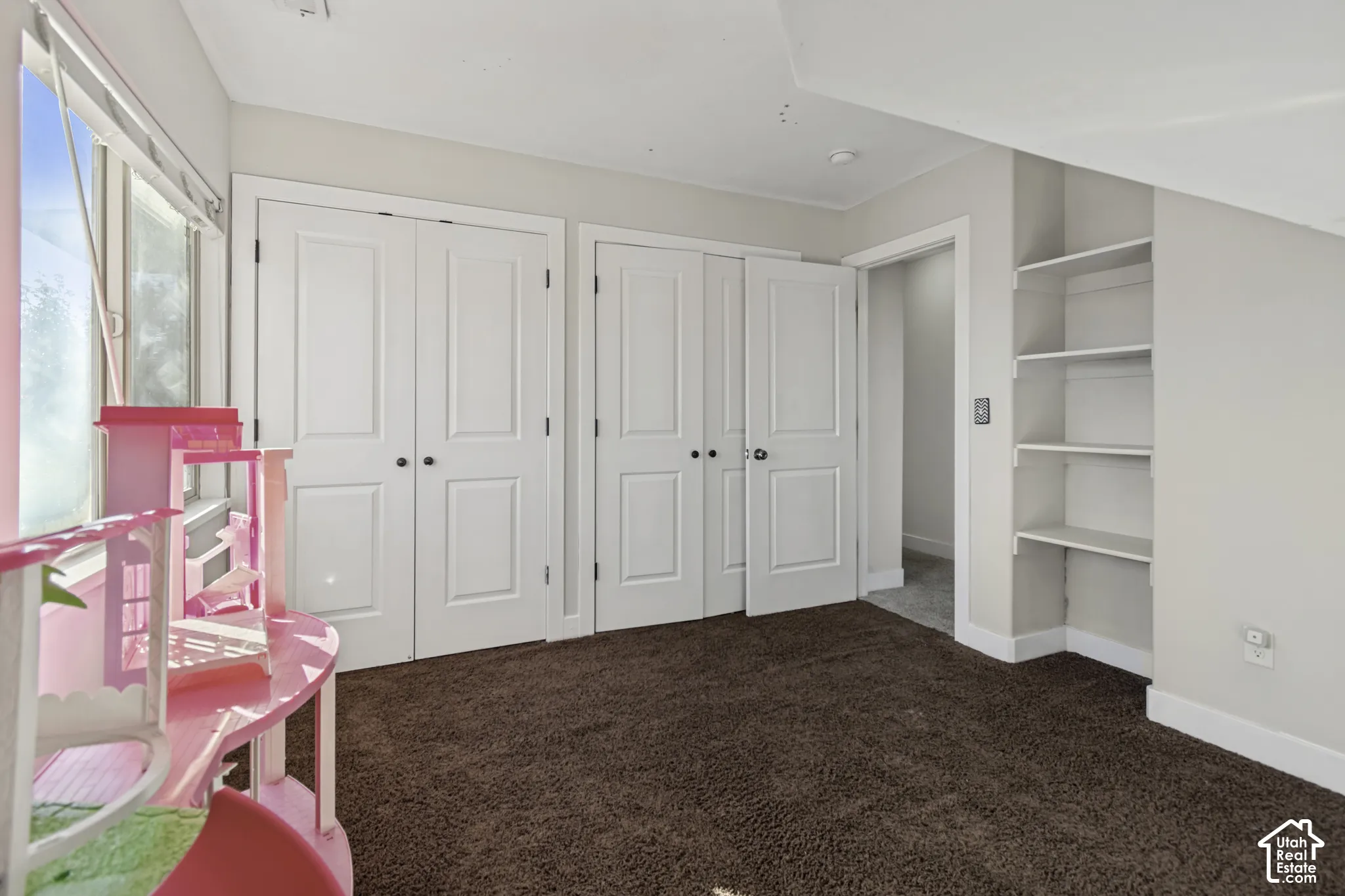 Room featuring neutral wall tones, textured carpeting, dual-panel closet doors, and built-in shelving