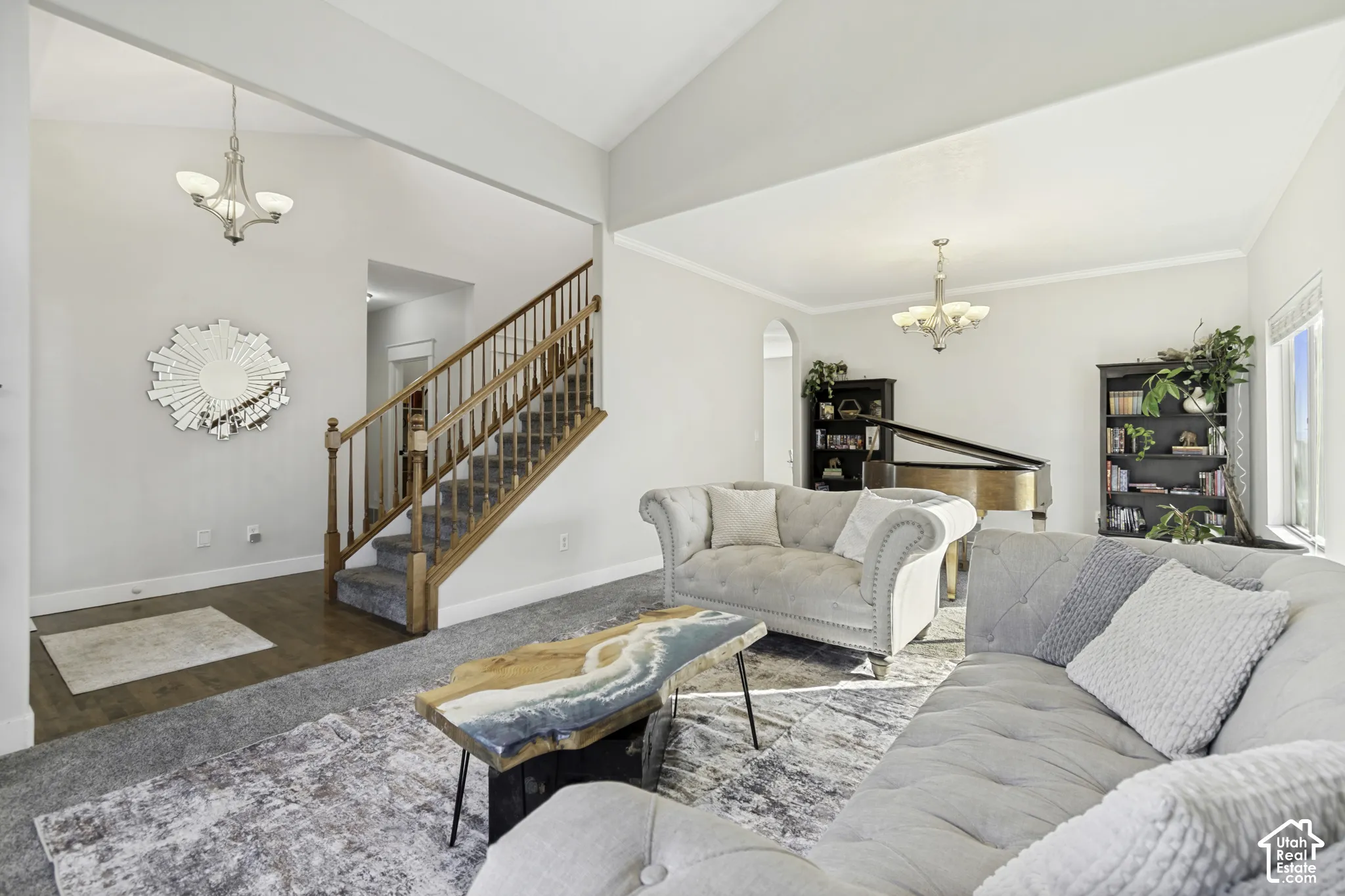 Vaulted ceilings, staircase with a wooden handrail and balusters, and dual tiered chandeliers