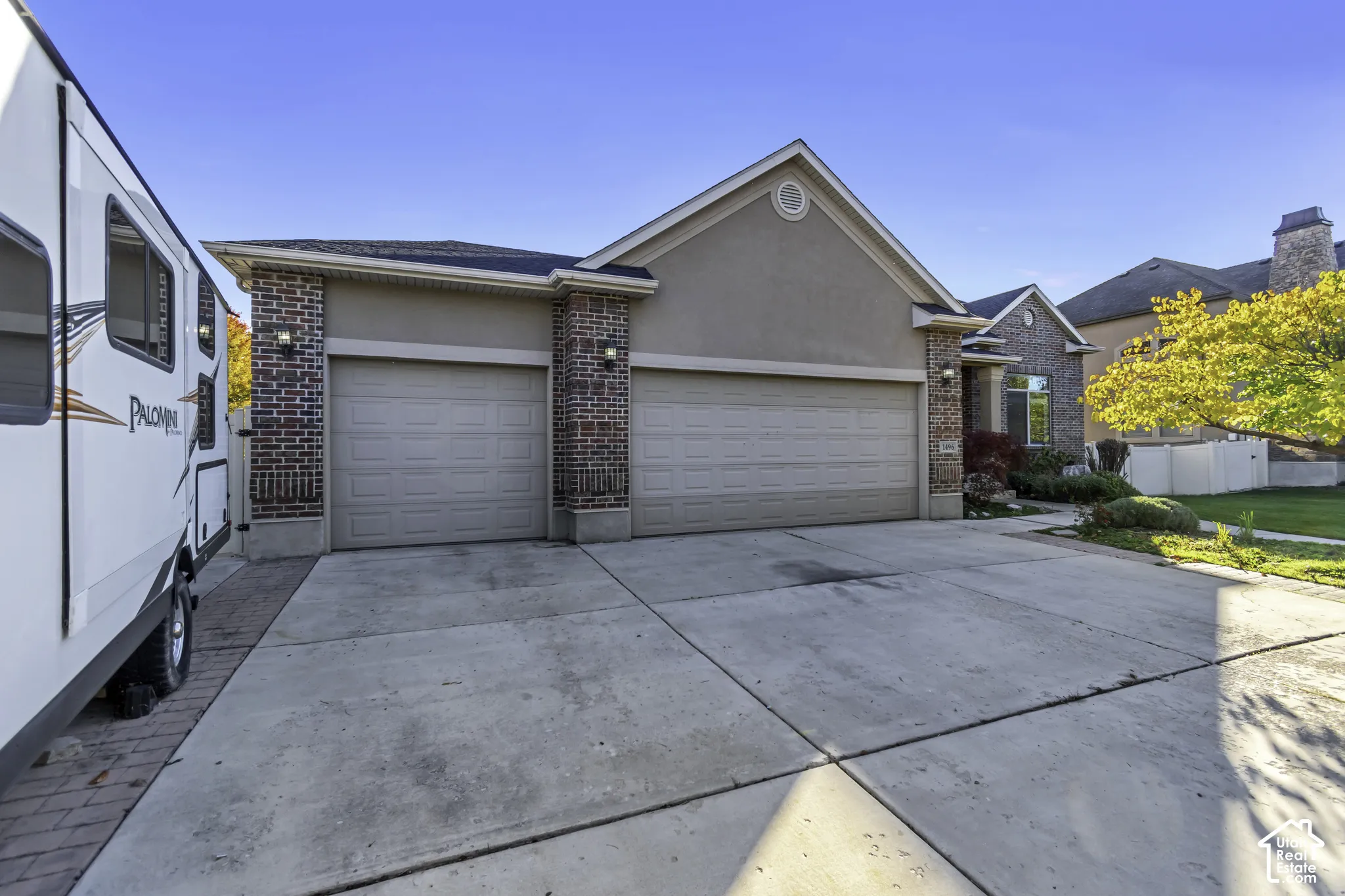 Exterior facade featuring a three-car garage, brick corner accents, stucco siding, and a concrete driveway