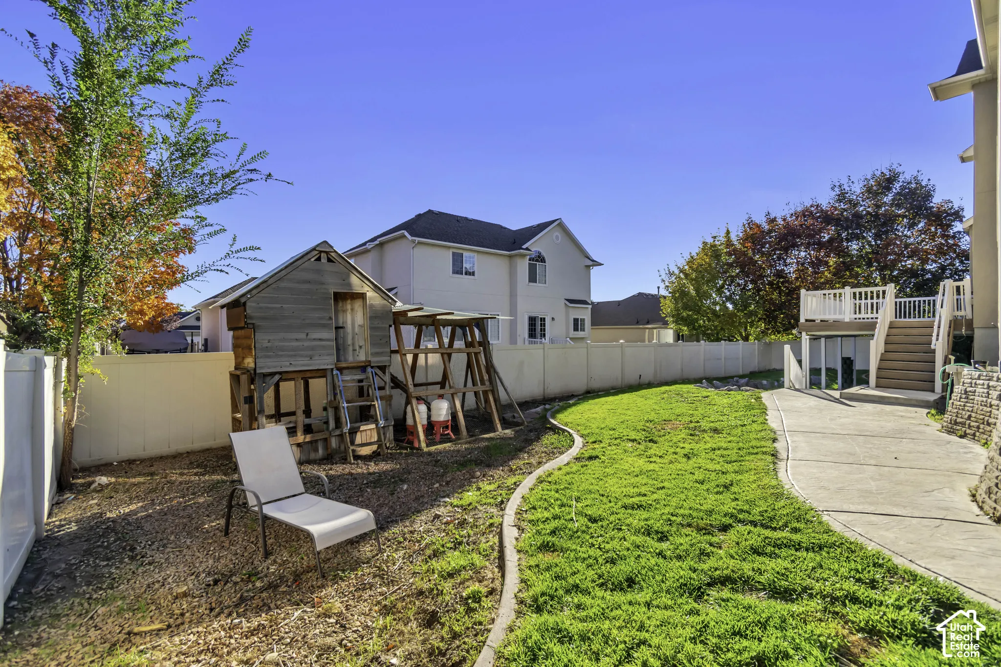 Backyard featuring a concrete patio, elevated wooden deck, vinyl privacy fencing, and a manicured lawn