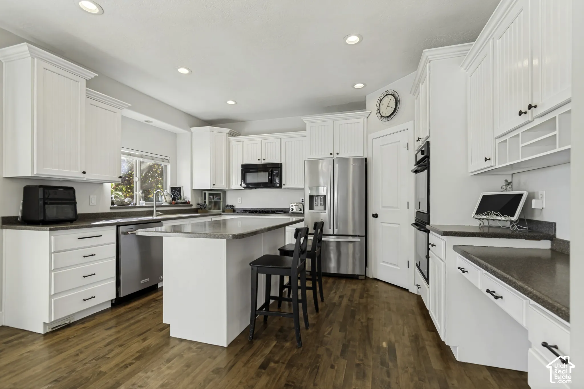 Kitchen featuring white cabinetry, center island with breakfast bar, stainless steel appliances, built-in dual ovens, and wood-finish flooring