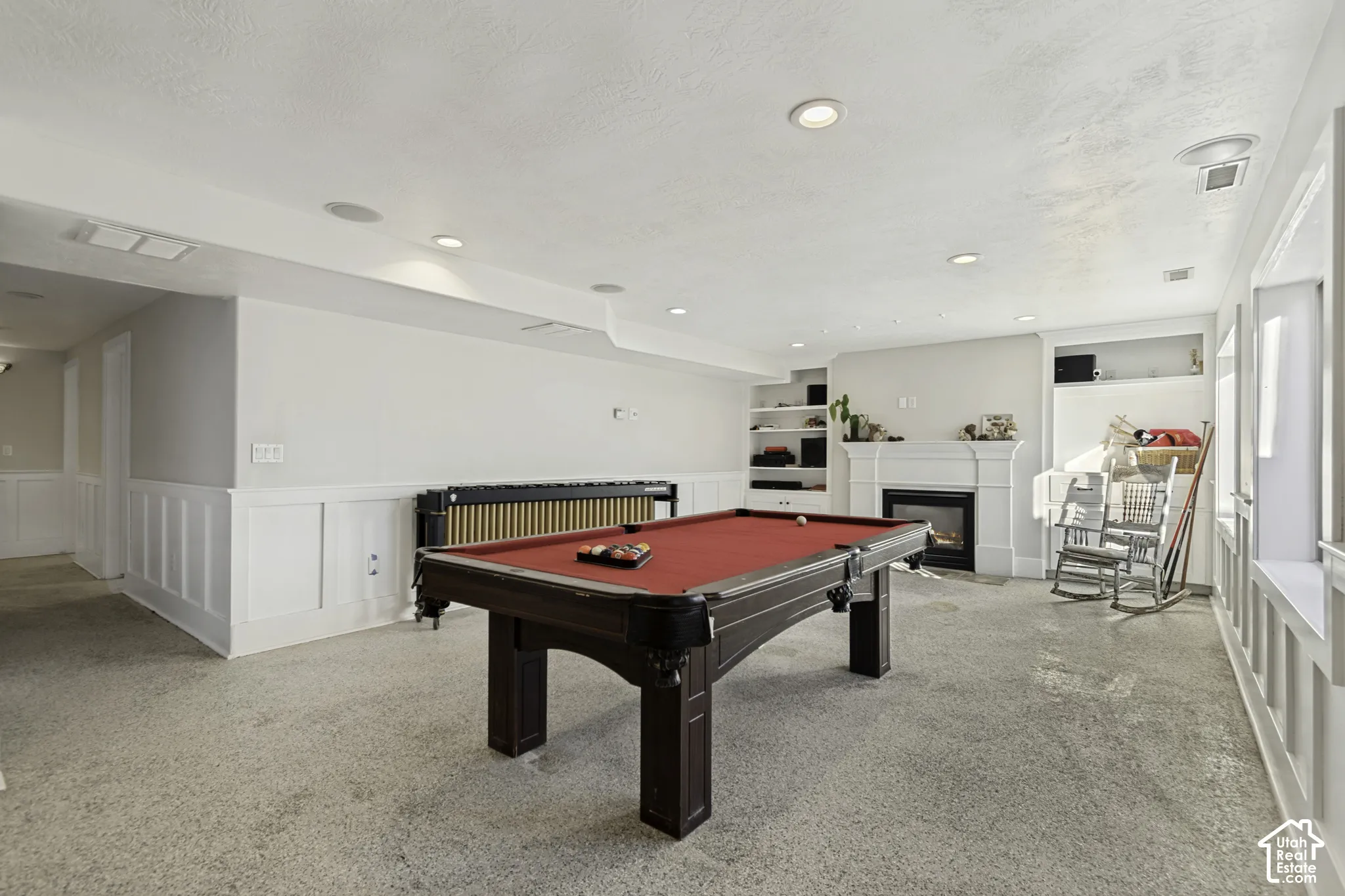 Spacious room featuring a fireplace with a decorative mantel, recessed lighting, built-in shelving, and wainscoting