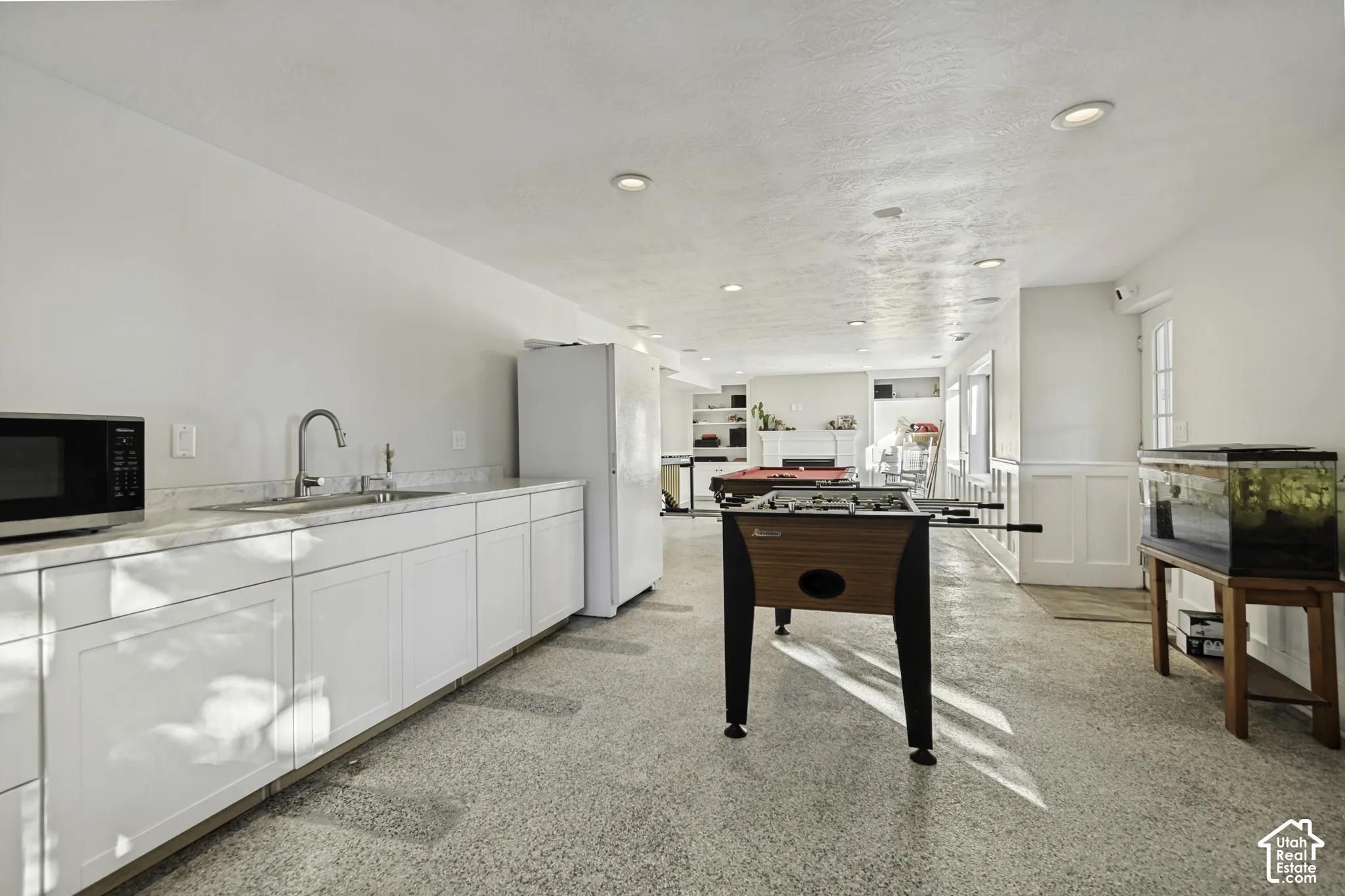 Kitchenette featuring white shaker-style cabinetry, solid-surface countertops, a stainless steel sink with an arched faucet, recessed lighting, and polished concrete flooring