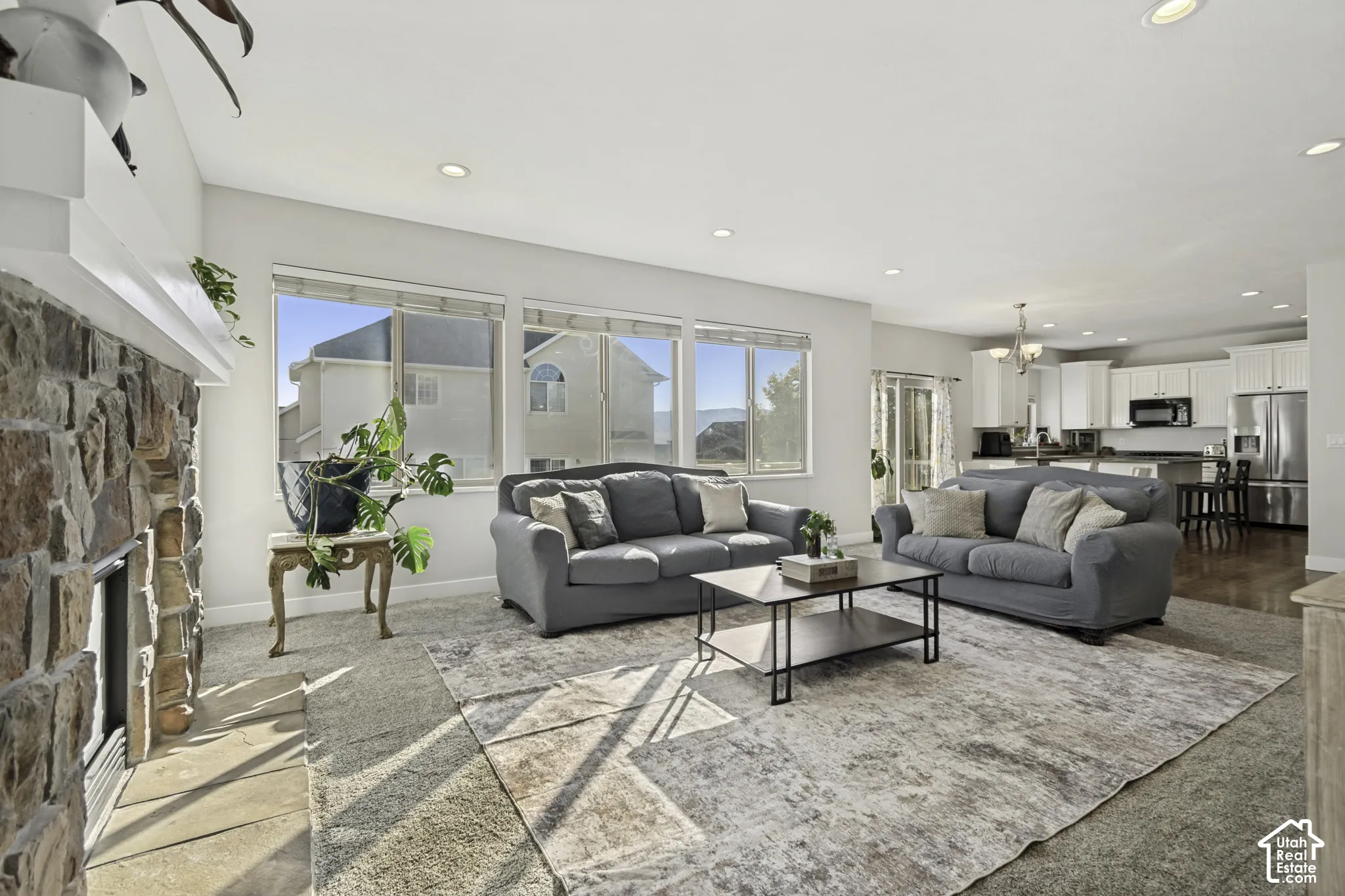 Living area featuring a floor-to-ceiling stone fireplace, recessed lighting, expansive picture windows, and wood-finish flooring throughout the kitchen area