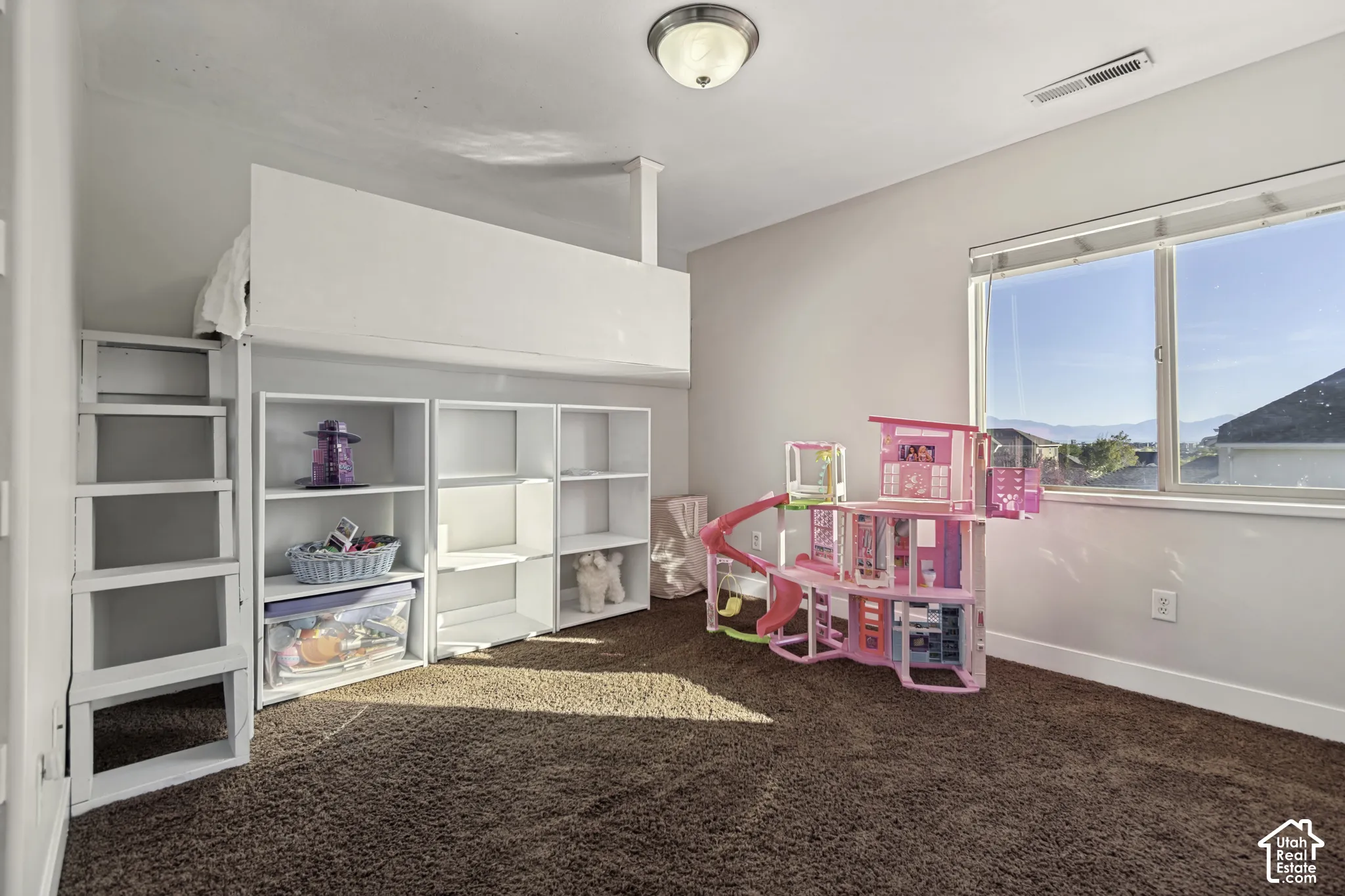 Interior room featuring neutral wall paint, wall-to-wall carpeting, a large window with blind, and built-in white shelving with an integrated loft structure