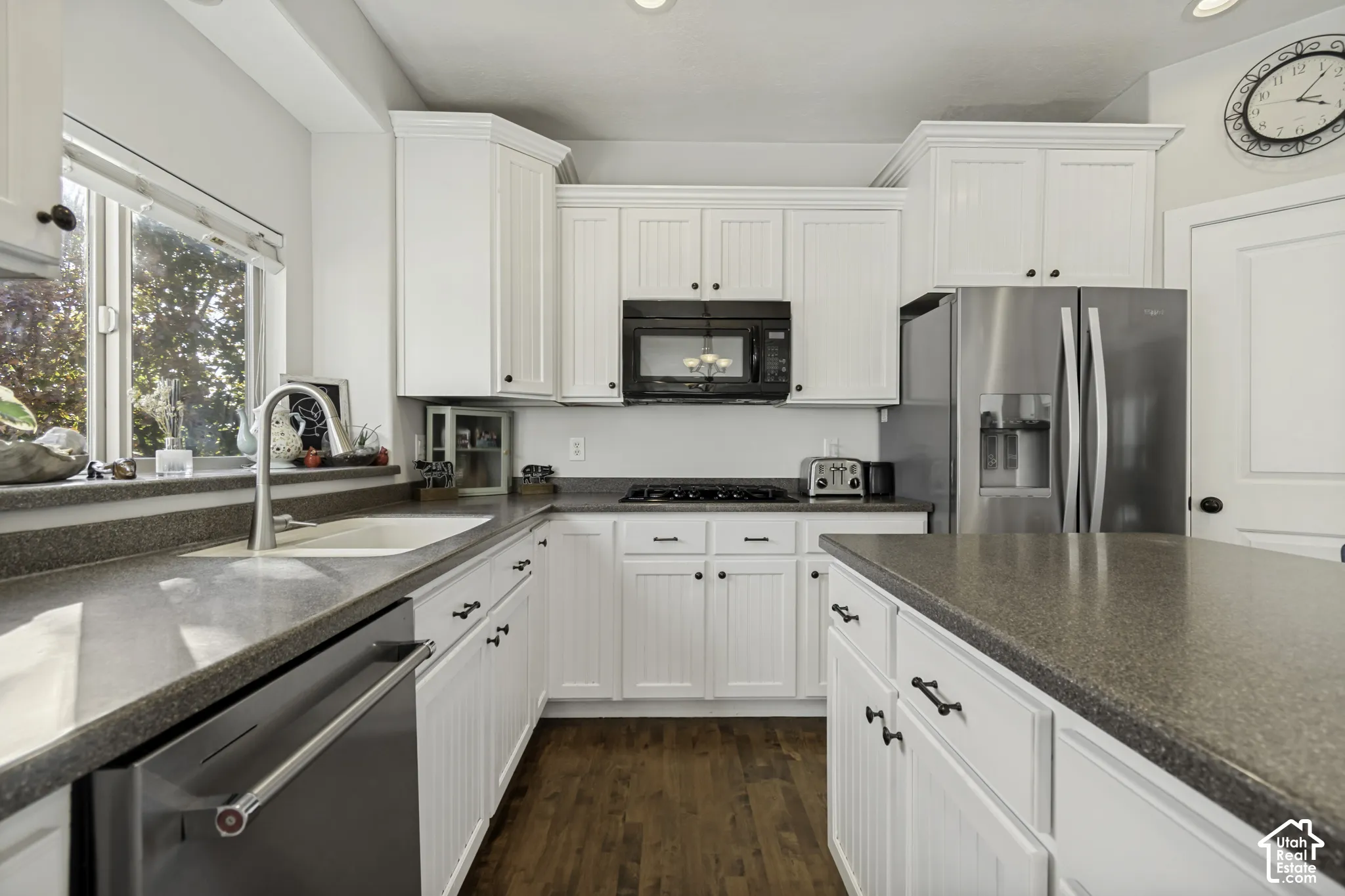 Kitchen featuring white shaker-style cabinetry, solid-surface countertops, wood-finish flooring, stainless steel appliances, and a undermount sink with a gooseneck faucet