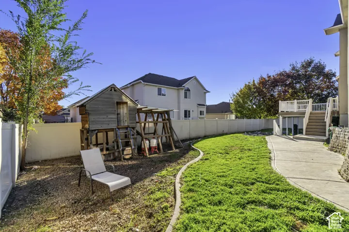 Backyard featuring a concrete patio, elevated wooden deck, vinyl privacy fencing, and a manicured lawn