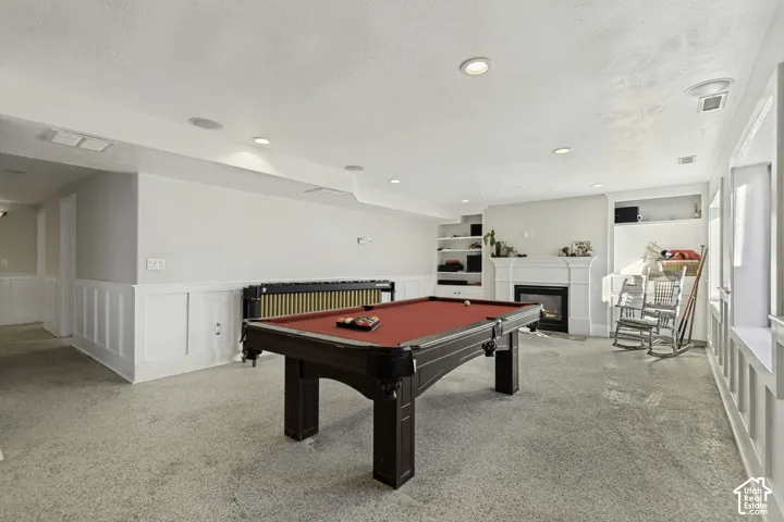 Spacious room featuring a fireplace with a decorative mantel, recessed lighting, built-in shelving, and wainscoting