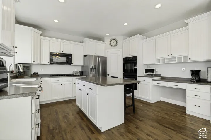 Kitchen featuring white shaker-style cabinetry, a center island, dark solid-surface countertops, wood-finish flooring, and a built-in double oven