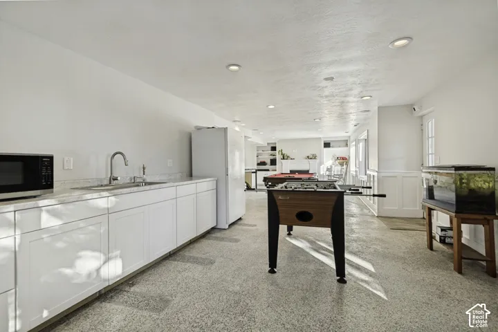 Kitchenette featuring white shaker-style cabinetry, solid-surface countertops, a stainless steel sink with an arched faucet, recessed lighting, and polished concrete flooring