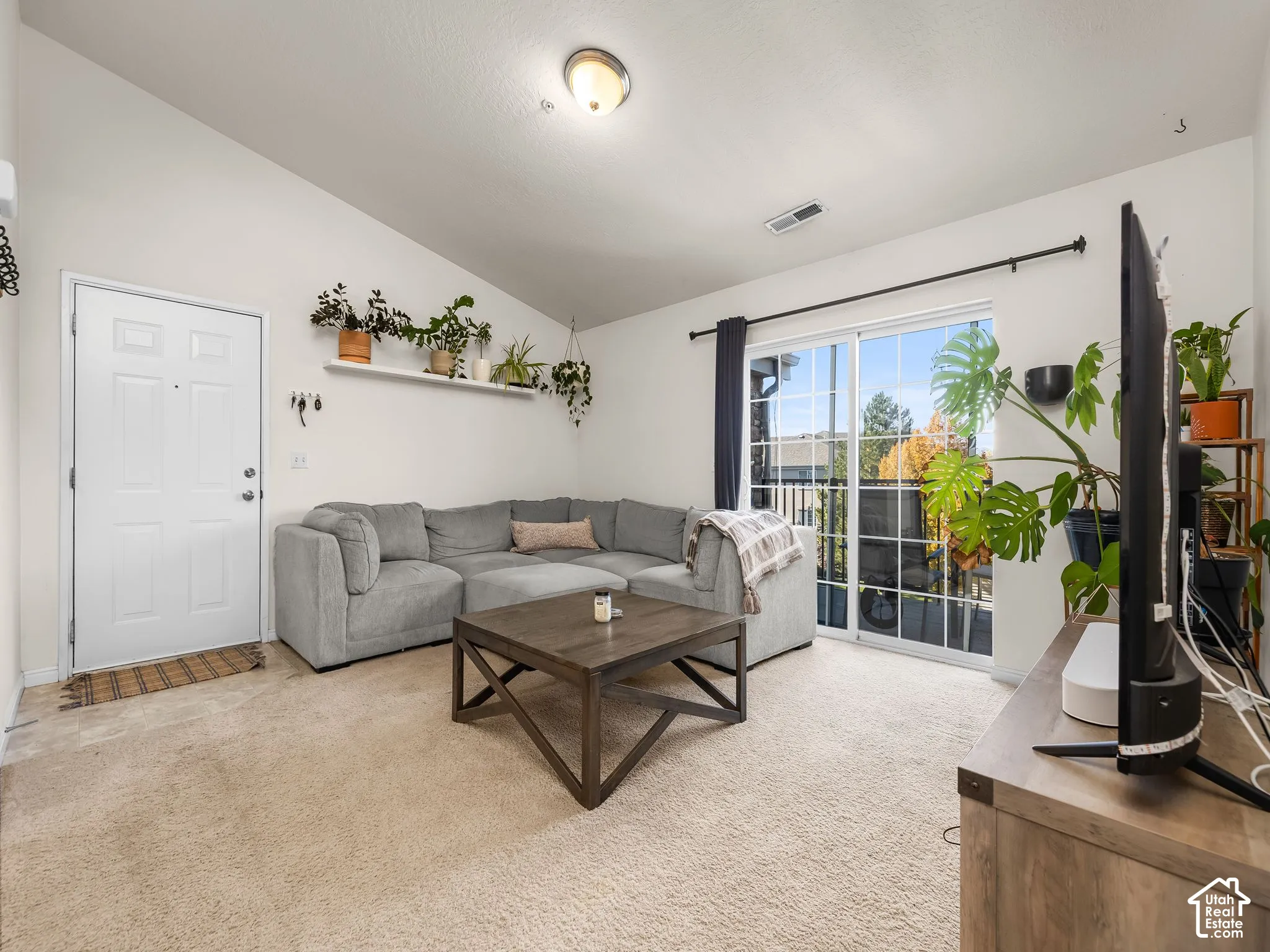 Vaulted ceilings, sliding glass door, built-in shelving, neutral carpeting, and flush-mount lighting fixture
