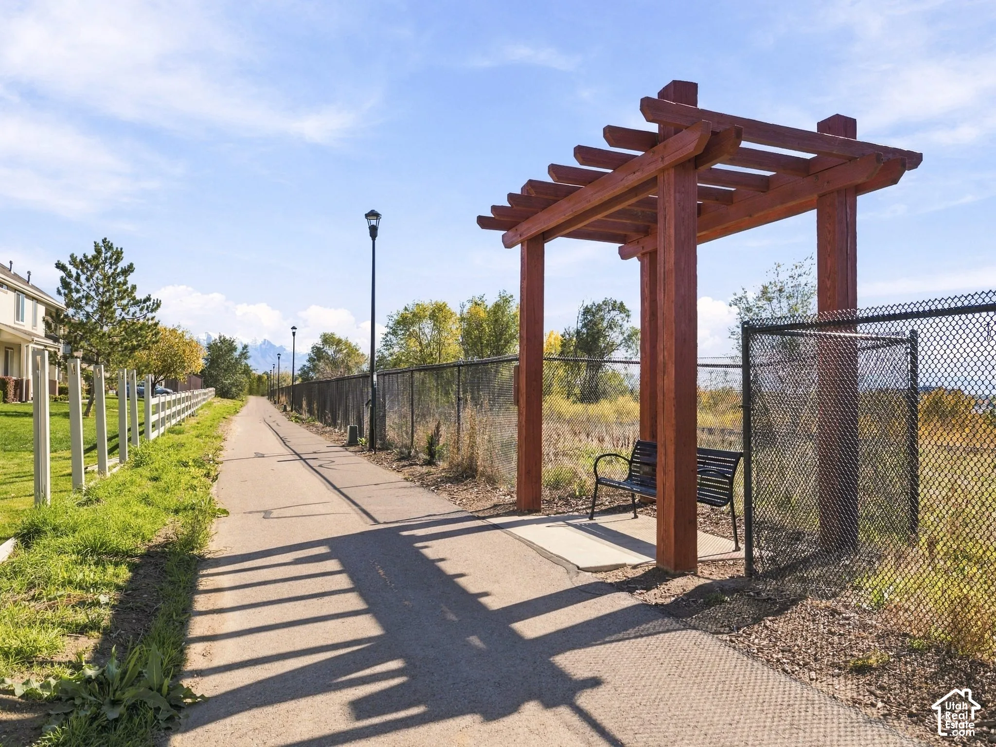 Paved pathway featuring a wood-beam pergola and outdoor lighting