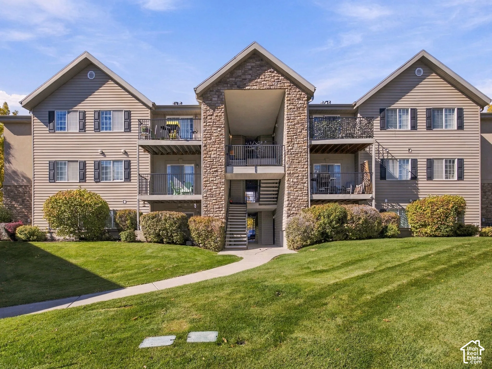 Multi-story residential building exterior featuring vinyl siding, stone-veneer accents, private balconies with metal railings, and a concrete walkway