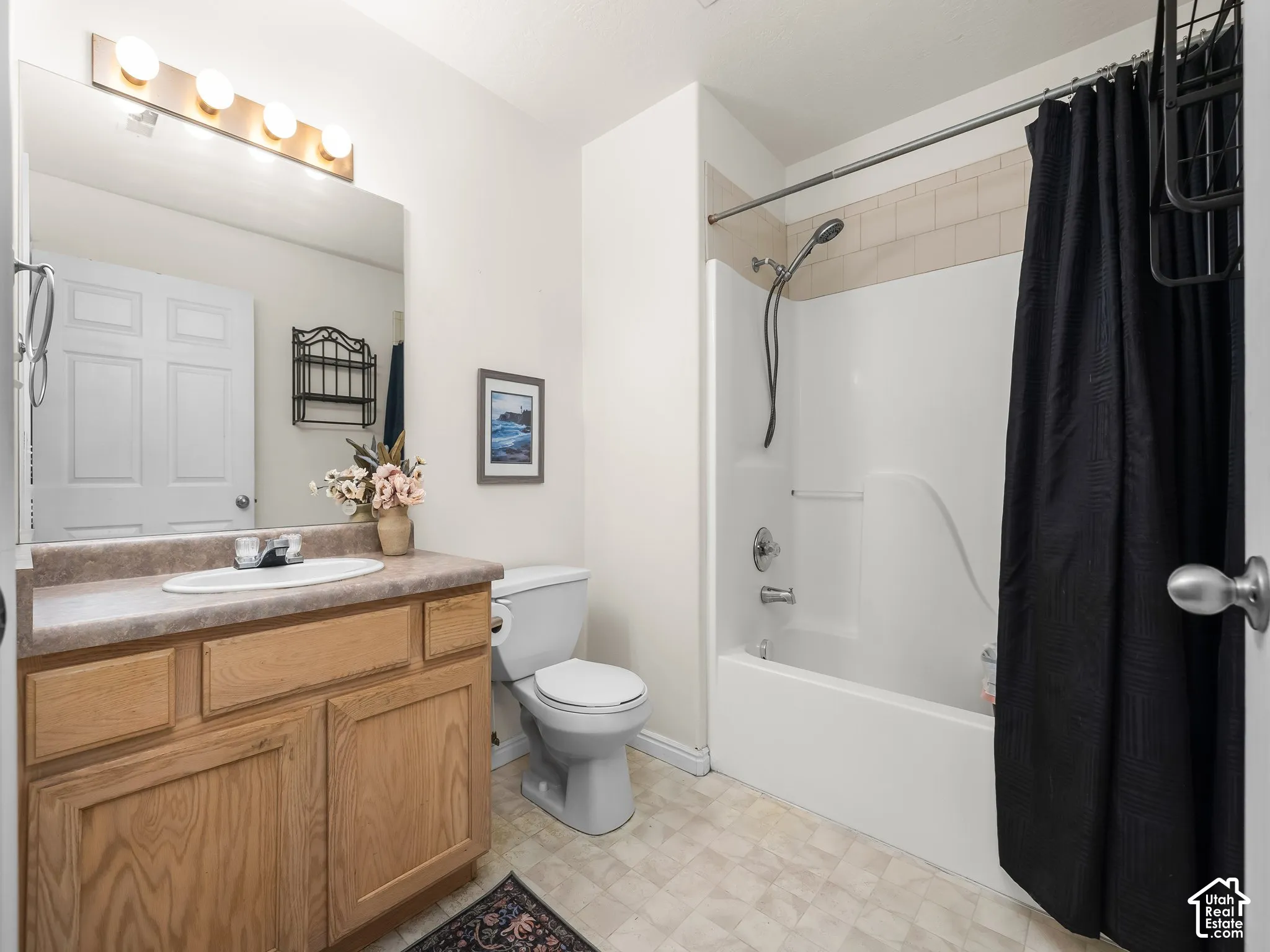 Wood-finish vanity with an integrated basin, large wall-mounted mirror, four-light fixture, and a tub-shower combination with a handheld showerhead