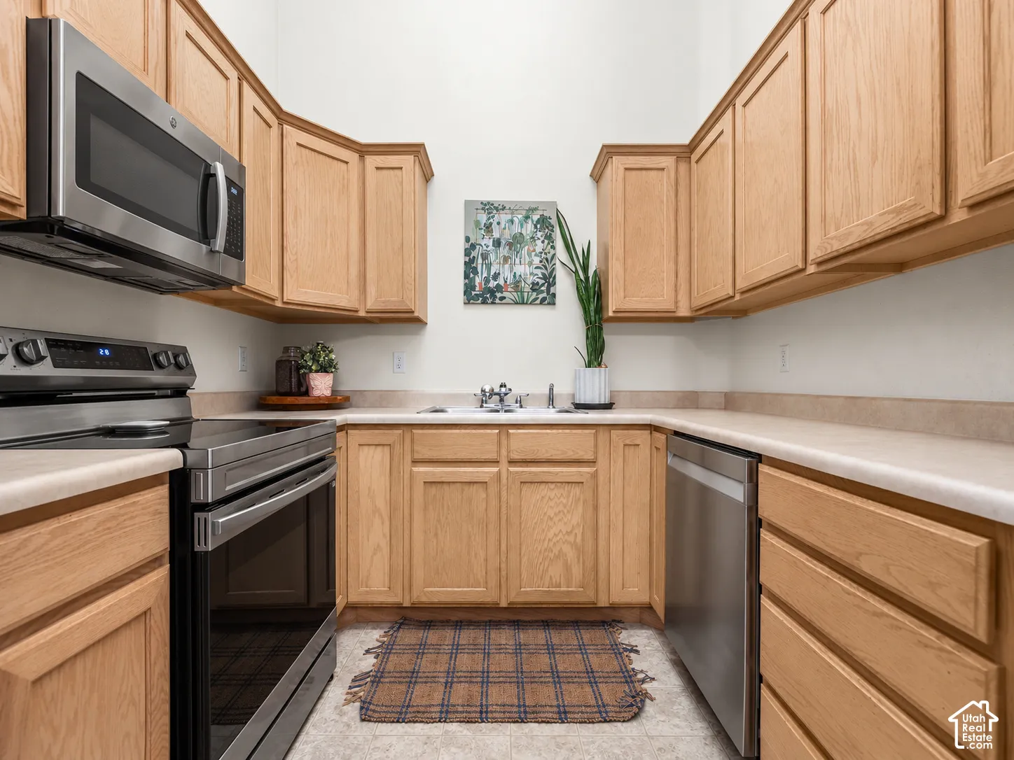 Galley-style kitchen featuring natural wood cabinetry, stainless steel appliances, neutral countertops with integrated backsplash, and high ceilings
