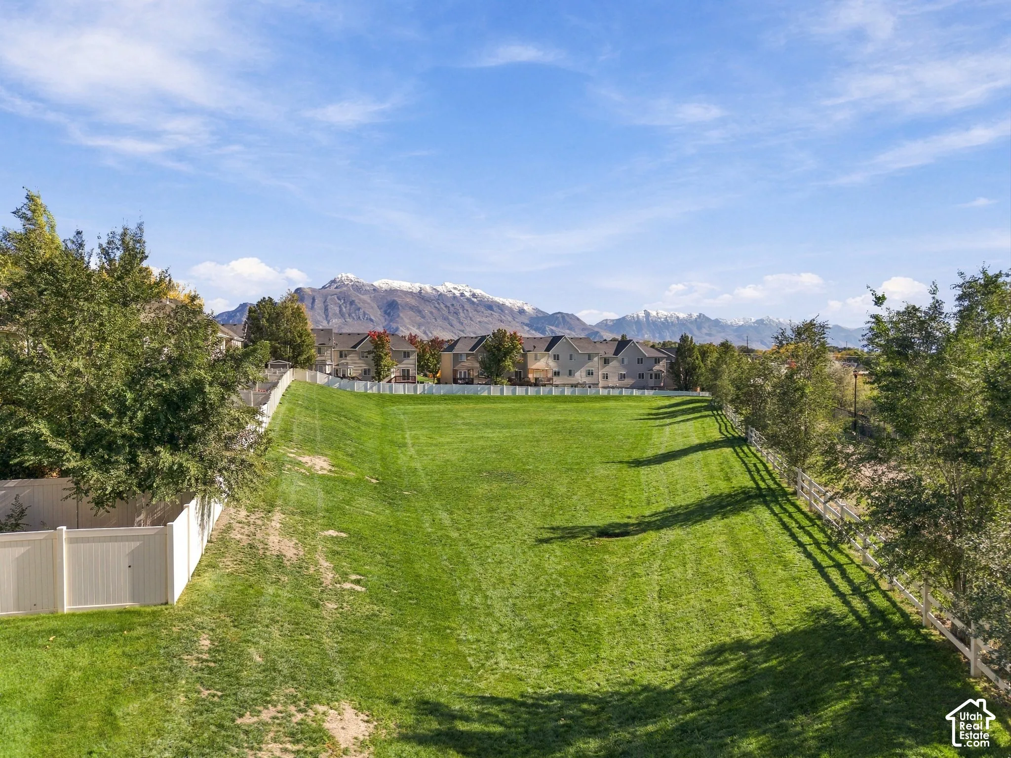 Expansive grassy lot featuring perimeter white vinyl fencing and a backdrop of snow-capped mountains
