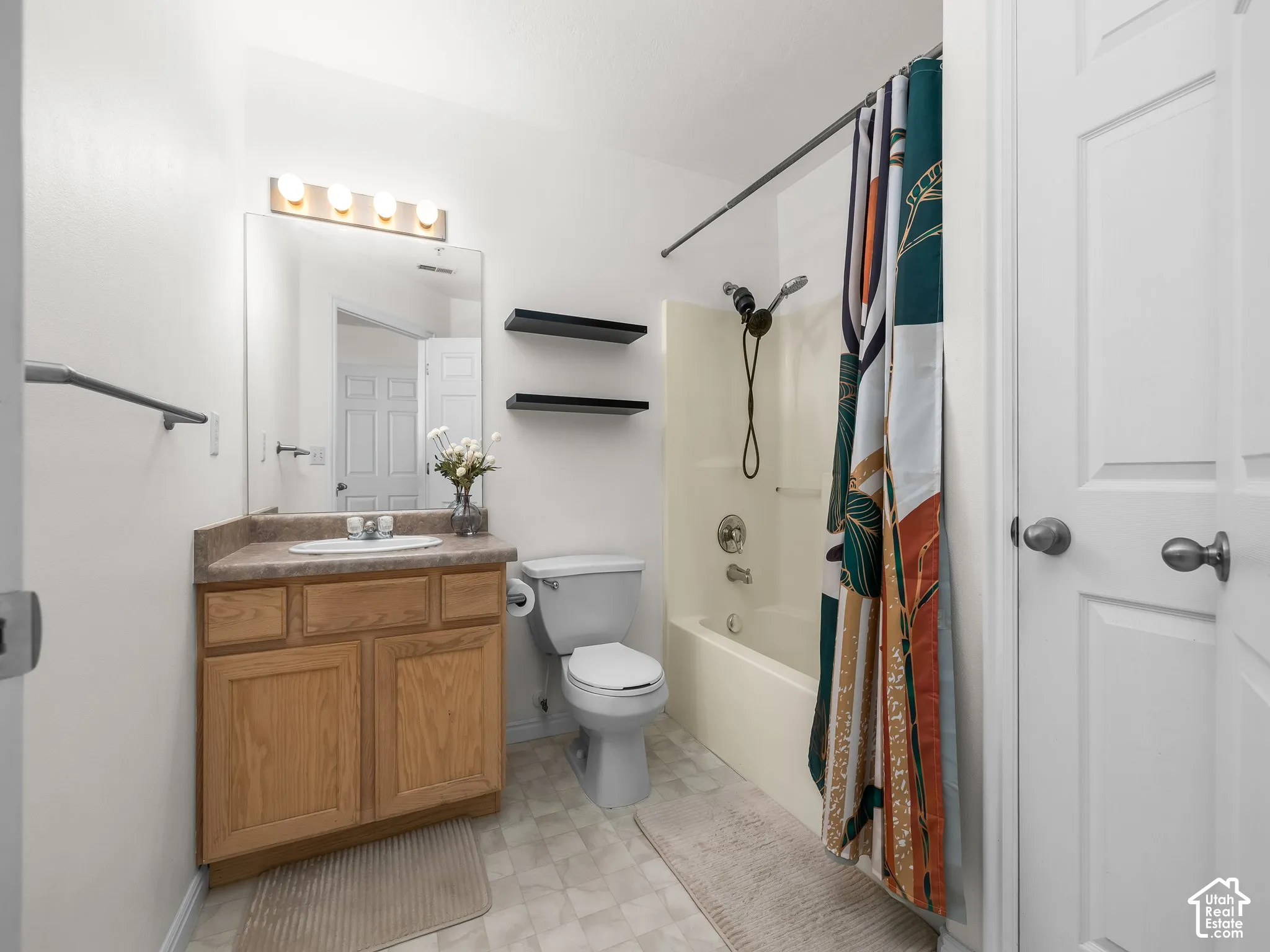 Bathroom featuring a wood-finish vanity with a stone-composite countertop, integrated sink, wall-mounted light fixture, and a combined tub and shower surround