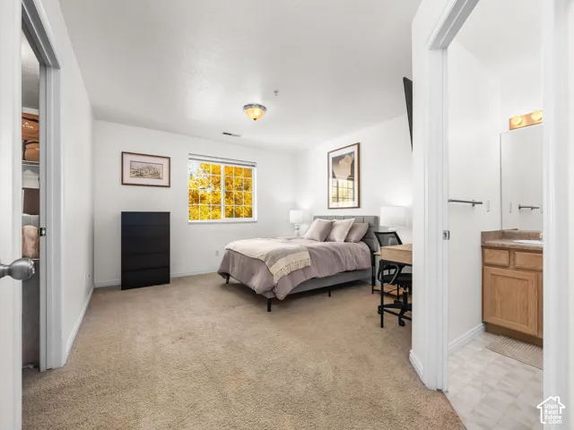 Bedroom with neutral carpeting, walk-in closet, and single-pane window, featuring a bathroom with a wood-finish vanity and stone-style countertop