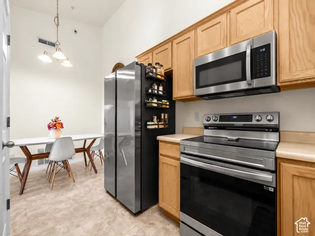 Kitchen featuring stainless steel appliances, wood cabinetry, stone-finish countertops, and a multi-light pendant fixture under a high ceiling