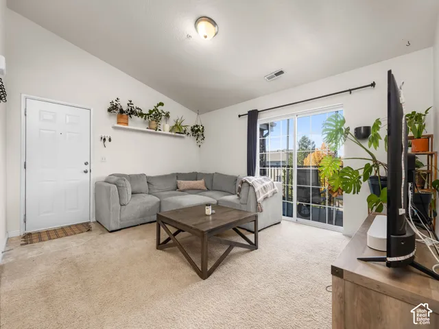 Vaulted ceilings, sliding glass door, built-in shelving, neutral carpeting, and flush-mount lighting fixture