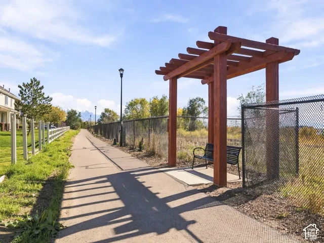 Paved pathway featuring a wood-beam pergola and outdoor lighting